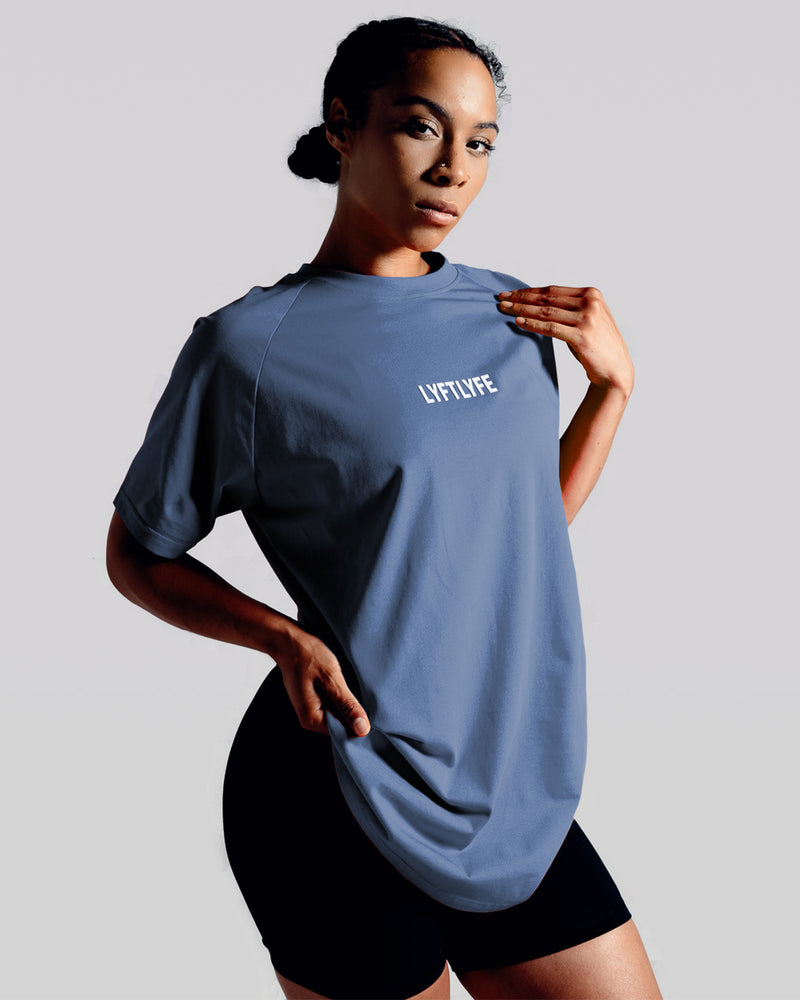 A female athlete is wearing a blue performance t-shirt with the Lyftlyfe logo in the center of the chest.