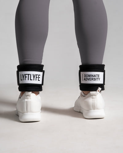 Person wearing white sneakers with black ankle bands displaying motivational phrases on a light gray background.