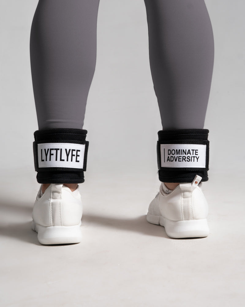 Person wearing white sneakers with black ankle bands displaying motivational phrases on a light gray background.