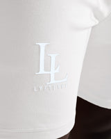 Close-up of LL LYFTLYFE logo printed on right thigh of light grey shorts.