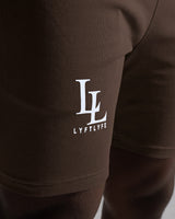 Close-up of LL LYFTLYFE logo printed on right thigh of dark brown shorts.