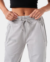 Close-up of the reflective Lyftlyfe logo on the right thigh of women’s light grey Breathe Joggers with a thick waistband.