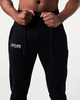 Close-up of black Breathe Joggers, showing elastic waistband, tonal drawstring, and Lyftlyfe reflective logo on the left thigh.