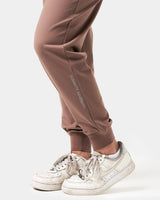 Close-up of the 'Dominate Adversity' slogan printed on the lower leg of women’s brown Breathe Joggers, showcasing attention to detail.