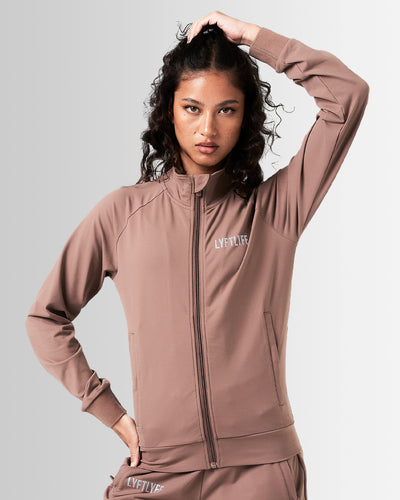 Front view of women’s Breathe Zip-Up Jacket in brown featuring a minimalist reflective Lyftlyfe logo on the left chest and a streamlined, athletic fit.
