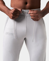 Close-up of light grey Breathe Joggers, showing elastic waistband, tonal drawstring, and Lyftlyfe reflective logo on the left thigh.