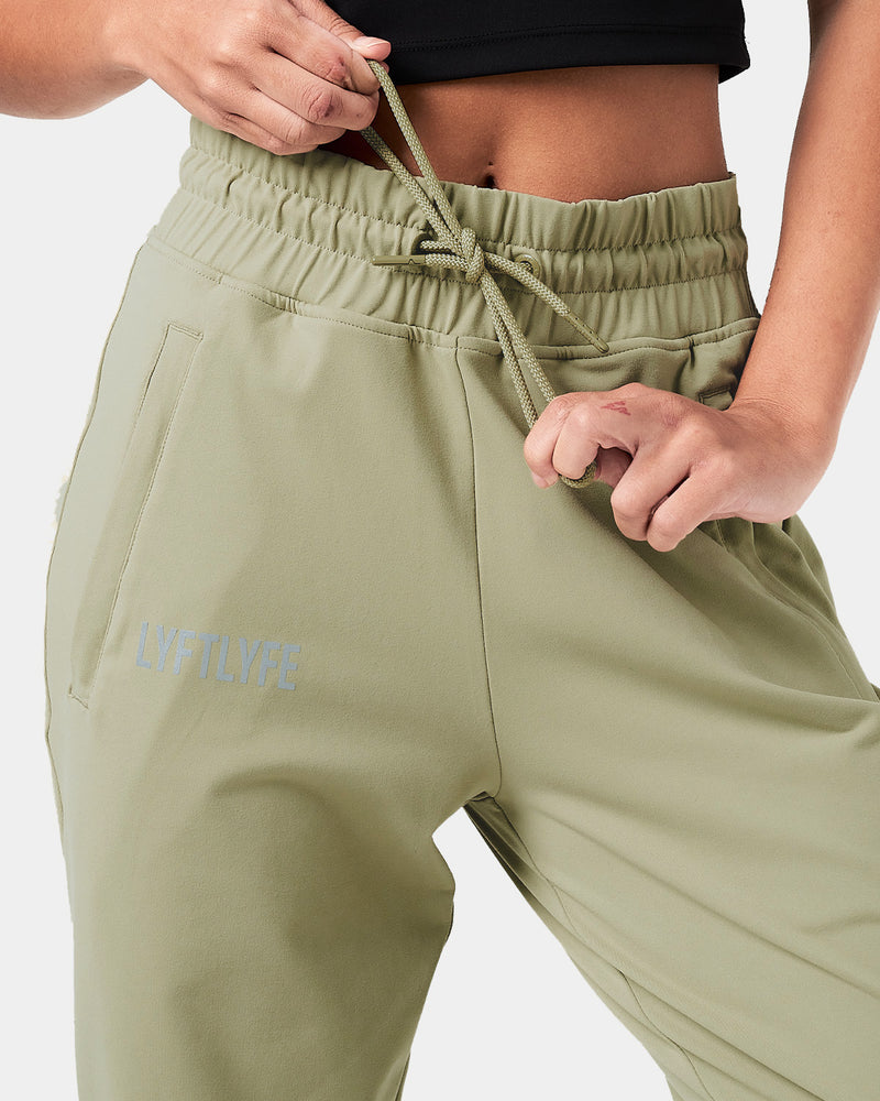 Close-up of the reflective Lyftlyfe logo on the right thigh of women’s green Breathe Joggers with a thick waistband.