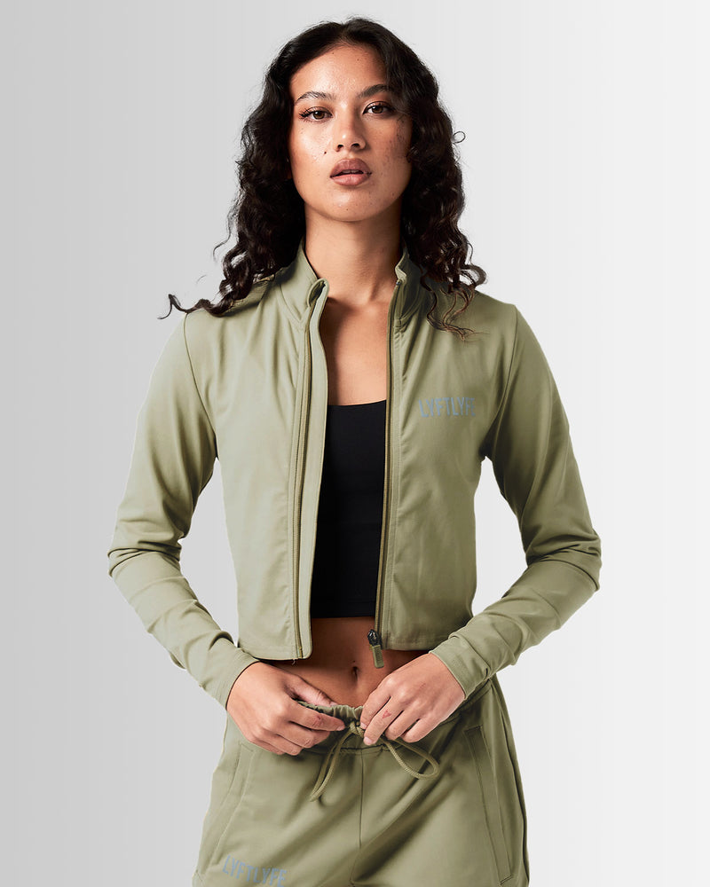 Front view of Breathe Women’s Zip-Up Crop in green with a reflective Lyftlyfe logo on the left chest and a flattering cropped fit.