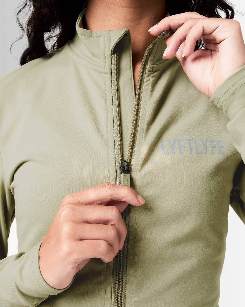 Front view of Breathe Women’s Zip-Up Crop in green with a reflective Lyftlyfe logo on the left chest and a flattering cropped fit.
