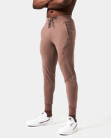 Left Side view of men’s Breathe Joggers in brown featuring the slogan 'Dominate Adversity' on the lower left leg and secure zippered pockets.