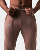 Close-up of brown Breathe Joggers, showing elastic waistband, tonal drawstring, and Lyftlyfe reflective logo on the left thigh.