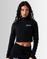 Front view of Breathe Women’s Zip-Up Crop in black with a reflective Lyftlyfe logo on the left chest and a flattering cropped fit.
