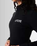 Close-up of the reflective Lyftlyfe logo on the left chest of the Breathe Women’s Zip-Up Crop in black, showcasing sleek branding.