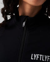 Close-up of the custom zipper closure on the Breathe Women’s Zip-Up Crop in black, featuring a sleek head cover and tonal stitching.