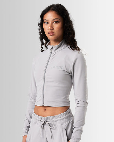 Front view of Breathe Women’s Zip-Up Crop in light grey with a reflective Lyftlyfe logo on the left chest and a flattering cropped fit.