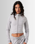 Front view of Breathe Women’s Zip-Up Crop in light grey with a reflective Lyftlyfe logo on the left chest and a flattering cropped fit.