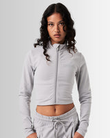 Front view of Breathe Women’s Zip-Up Crop in light grey with a reflective Lyftlyfe logo on the left chest and a flattering cropped fit.