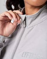 Close-up of the custom zipper closure on the Breathe Women’s Zip-Up Crop in light grey, featuring a sleek head cover and tonal stitching.