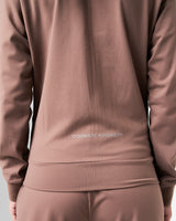 Close-up of the lower back slogan 'Dominate Adversity' on women’s lightweight brown zip-up jacket.