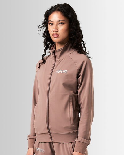 Front view of women’s Breathe Zip-Up Jacket in brown featuring a minimalist reflective Lyftlyfe logo on the left chest and a streamlined, athletic fit.