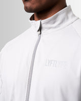 Close-up of the custom zipper detailing on men’s light grey Breathe Jacket, highlighting tonal stitching and technical craftsmanship.