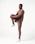 Side profile of brown men’s joggers with a reflective slogan near the pocket and stretch fabric for optimal movement.