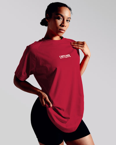 A female athlete is wearing a red performance t-shirt with the Lyftlyfe logo in the center of the chest.