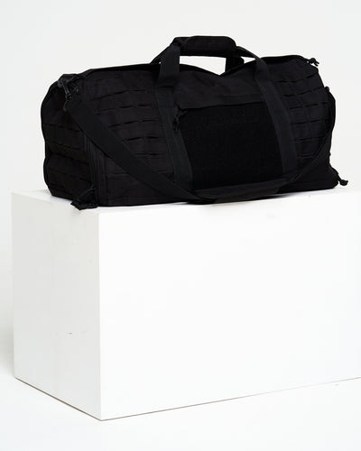 Black duffel bag on a white cube with a white background