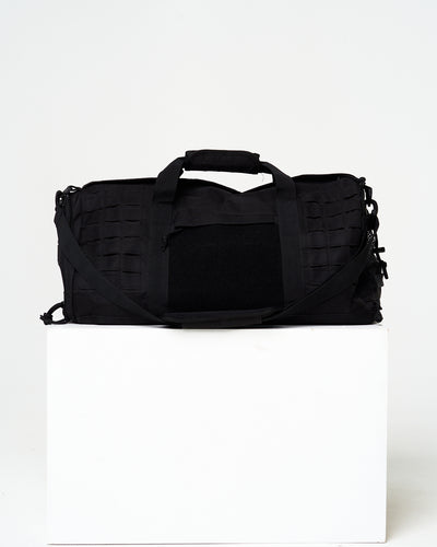 Black duffel bag on a white cube with a white background