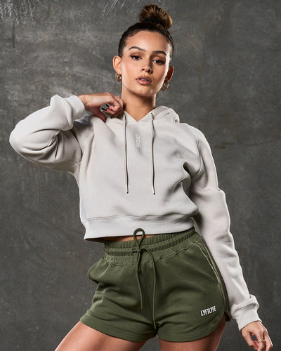 Women’s fleece cropped hoodie in sand, front shot with clean silhouette and central logo.
