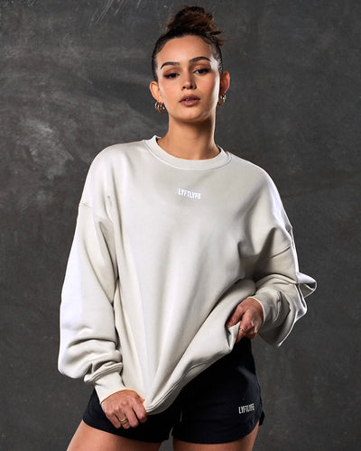 Oversized women's crewneck in off-white with a brand logo on a light gray background