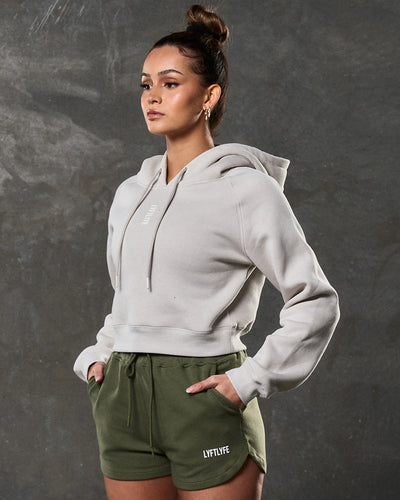 Women’s fleece cropped hoodie in sand, front shot with clean silhouette and central logo.