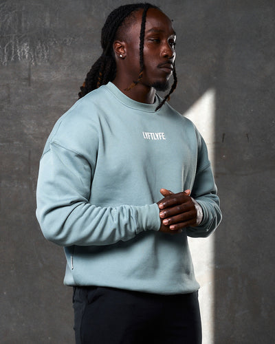 Front-facing men’s light blue crewneck featuring ribbed cuffs, a centered Lyftlyfe logo, and ultra-plush fleece for comfort.