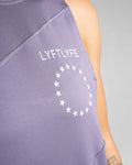 Close-up of white Lyftlyfe logo on the left chest of Women’s Dominance Cut Sleeve tank in purple. 