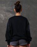 Back view of women’s black oversized crewneck with ultra-soft fleece fabric, ribbed hem, and relaxed fit.