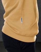 Dominate flag tag detail on yellow hoodie above kangaroo pocket seam.