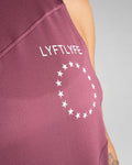 Close-up of white Lyftlyfe logo on the left chest of Women’s Dominance Cut Sleeve tank in prune.  
