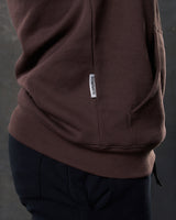 Dominate flag tag detail on brown hoodie above kangaroo pocket seam.