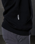 Dominate flag tag detail on black hoodie above kangaroo pocket seam.