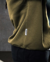 Detailed side view of the Lyftlyfe flag tag featuring 'Dominate Adversity' slogan on men's green fleece crewneck.