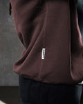 Close-up of the side flag tag with 'Dominate Adversity' slogan on the men's dark brown oversized Adapt Crew. 