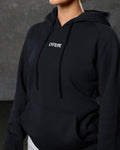 Close-up of center front logo and tonal drawstrings on women’s hoodie in black
