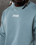 Close-up of the white Lyftlyfe logo on the chest of men’s light blue oversized Adapt Crew.