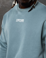 Close-up of the white Lyftlyfe logo on the chest of men’s light blue oversized Adapt Crew.