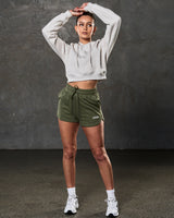 Full outfit view with fleece crop hoodie in sand and green workout shorts.