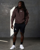 Full-body shot of man in LYFTLYFE brown hoodie and black shorts, standing confidently.