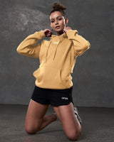 Lifestyle shot of women’s yellow hoodie styled with black athletic shorts.