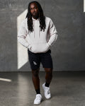 Full-body shot of man in LYFTLYFE hoodie in white sand and black gym shorts.
