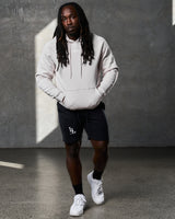Full-body shot of man in LYFTLYFE hoodie in white sand and black gym shorts.

