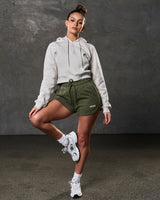 Full body shot of cropped hoodie in sand paired with green athletic shorts.